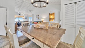 Uma ampla área de jantar com mesa e cadeiras de madeira, um candelabro e vista para a cozinha e a sala de estar.