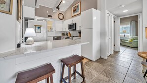 Cozinha moderna com armários brancos, ilha de mármore e área de jantar com dois banquinhos de madeira.