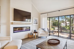 A modern living room with a fireplace, a sofa, a coffee table, and a view of the outdoors.