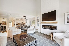 A spacious living room with a fireplace, a dining area, and a kitchen in the background.