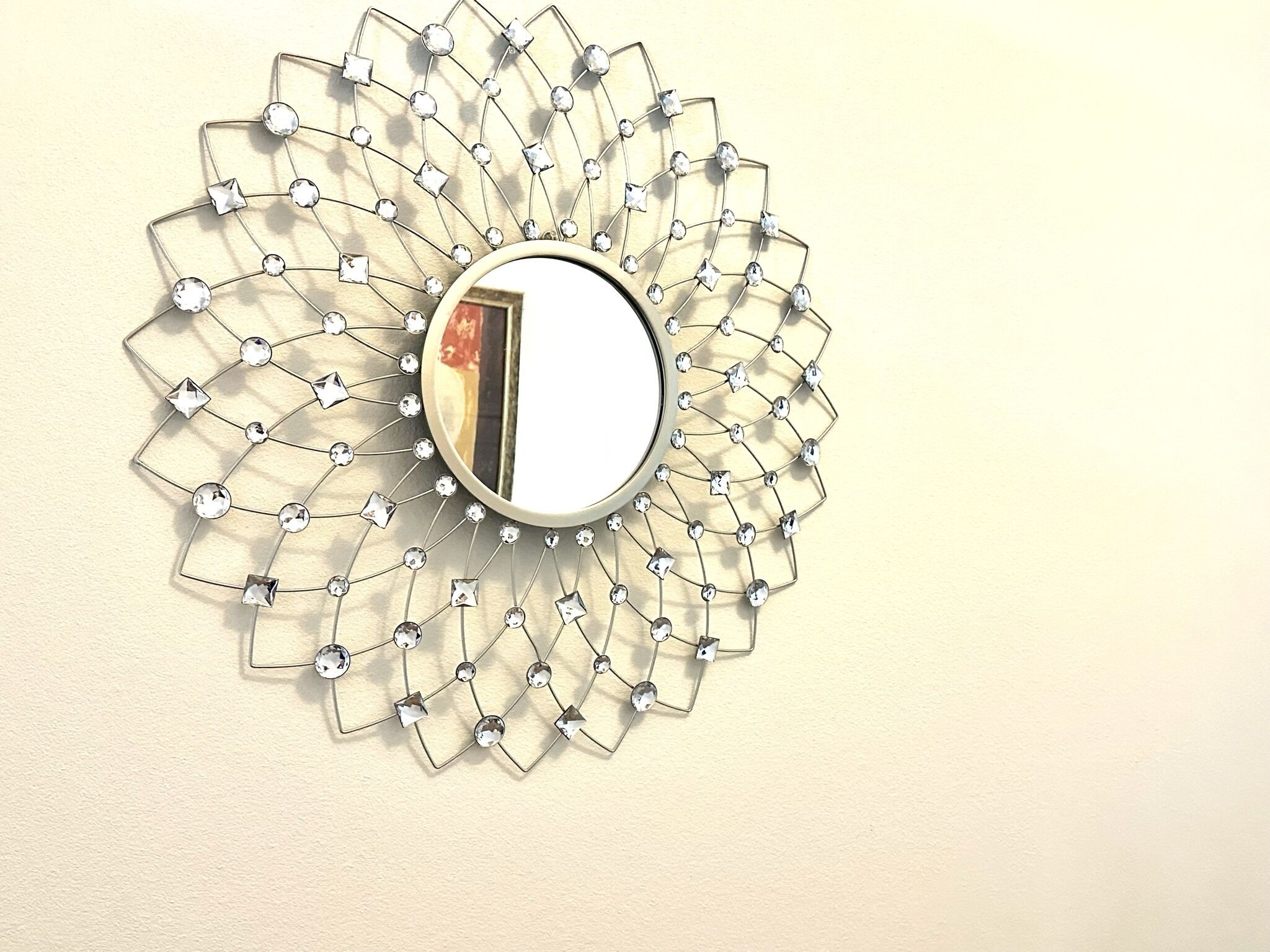Un miroir mural doté d’un cadre géométrique en métal et de nombreux ornements en cristal transparent.