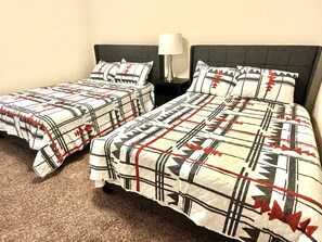 Two single beds with matching headboards and footboards, a bedside table with a lamp, and a carpeted floor.