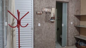 A room with a white door, a red coat rack, a small shelf with a decorative item, and a bathroom visible through an open door. - Spacious suites near Tabatinga Beach (Ubatuba)