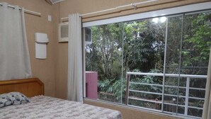 A bedroom with a bed, a window, a curtain, and an air conditioning unit. - Spacious suites near Tabatinga Beach (Ubatuba)
