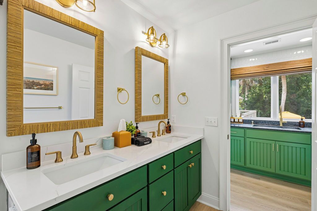 A bathroom with a white sink, gold fixtures, green cabinets, and a large mirror with gold trim.