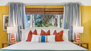 A hotel room with a large bed, striped curtains, a window with a view of trees, and two bedside lamps. - Pvt Pool/Spa-Game Room-Theater-Cold Plunge-Sauna-2min Walk to Beach (Hilton Head Island)