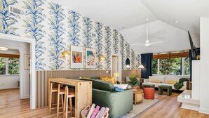 A modern living room with a green sofa, wooden dining table, and a wall with blue floral wallpaper. - Pvt Pool/Spa-Game Room-Theater-Cold Plunge-Sauna-2min Walk to Beach (Hilton Head Island)