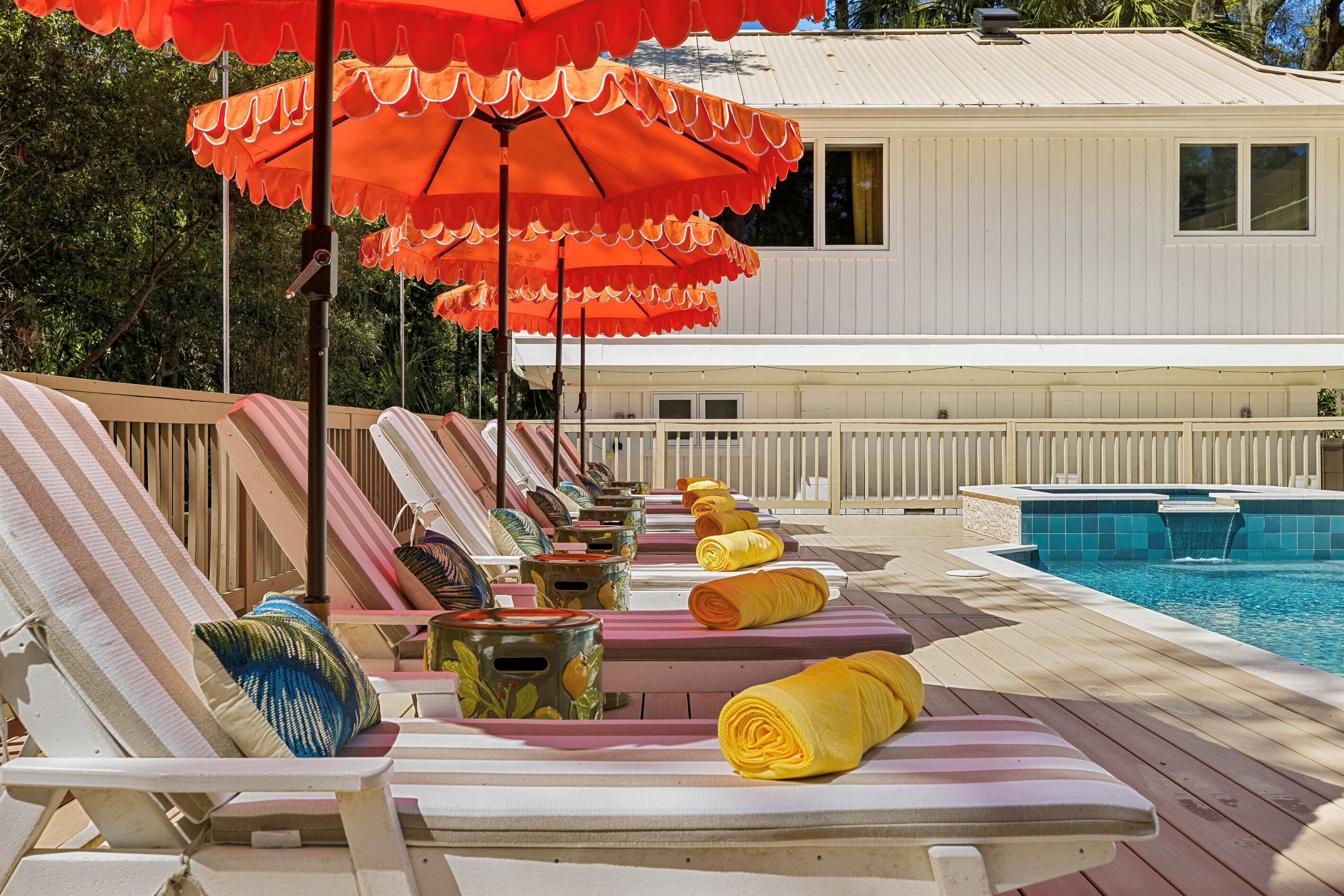 Zona junto a la piscina con sillas de descanso, sombrillas y una pileta.