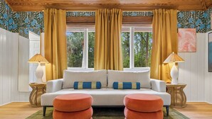 A room with a sofa, two lamps, a window with curtains, and a patterned wall. - Pvt Pool/Spa-Game Room-Theater-Cold Plunge-Sauna-2min Walk to Beach (Hilton Head Island)