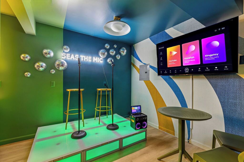 A recording studio with a neon sign, a large screen, and a laptop on a table.