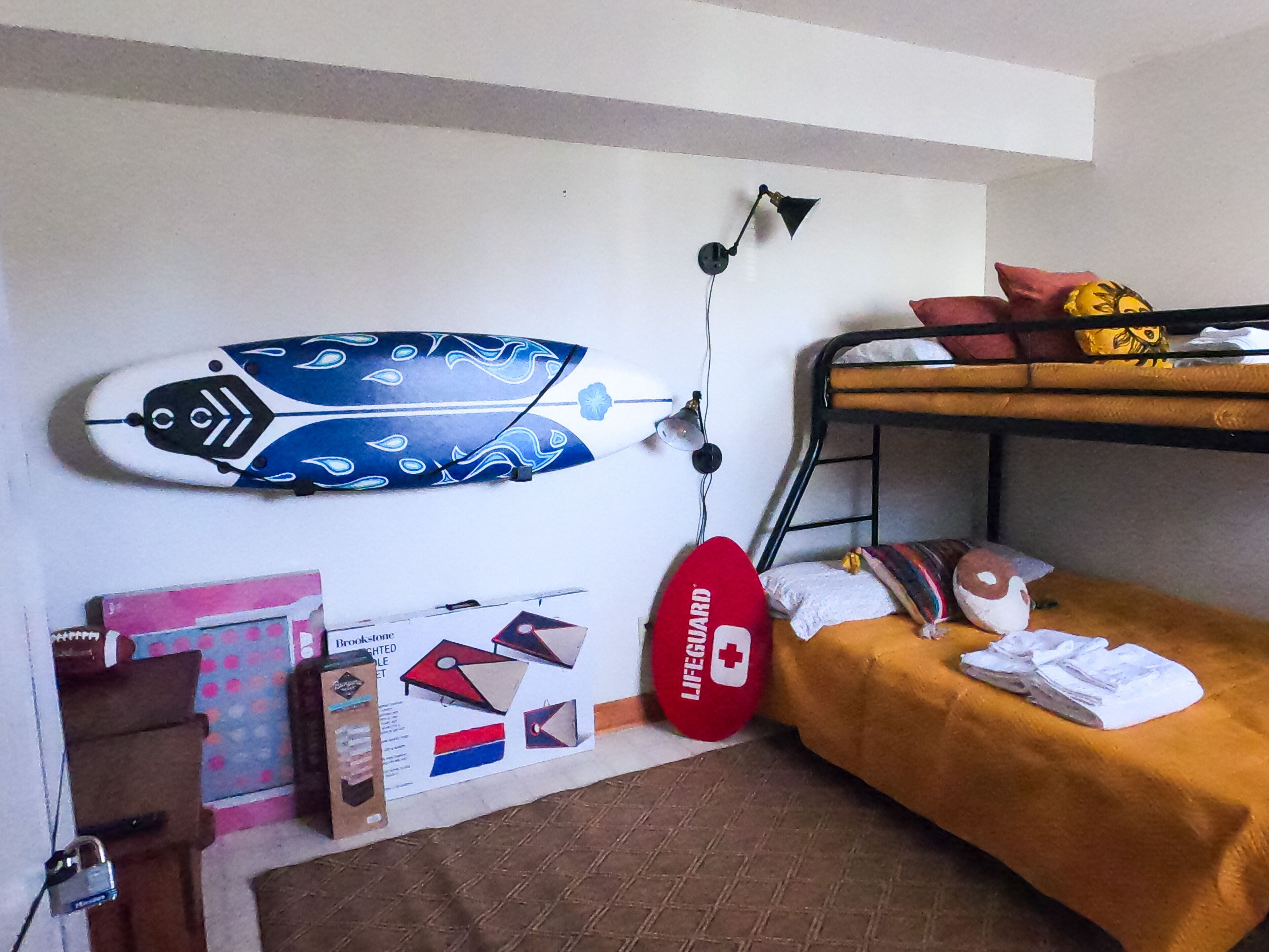 A dormitory room with bunk beds, a surfboard, a lamp, and some books.