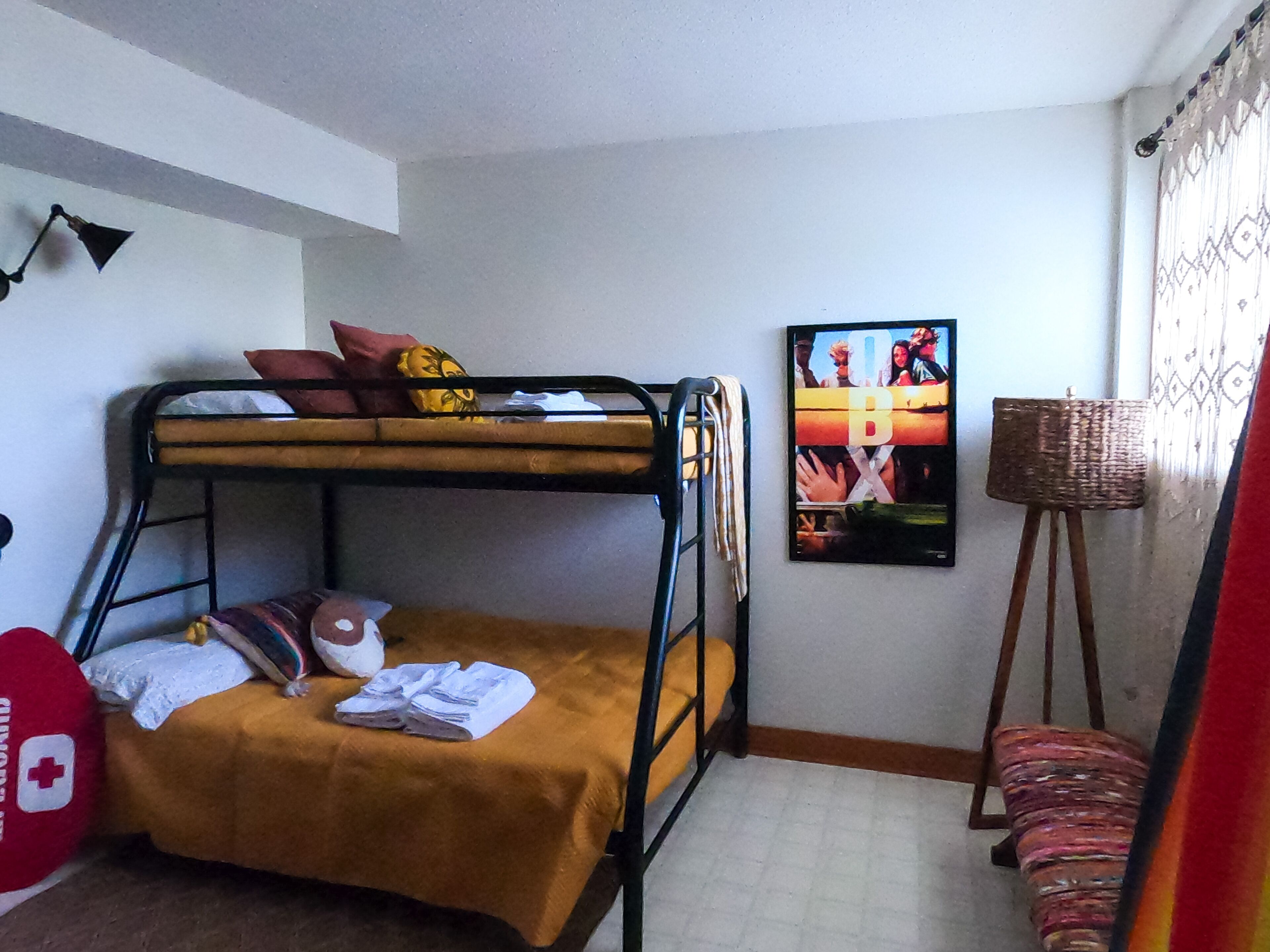 A bunk bed with pillows and blankets, a small table, a chair, and a poster on the wall.