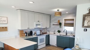 A modern kitchen with white cabinets, a central island with bar stools, a microwave, a stove, and a sink. - 500 feet to the Beach, Full house with Stocked Kitchen, Linens & Beach Supplies (Avon)