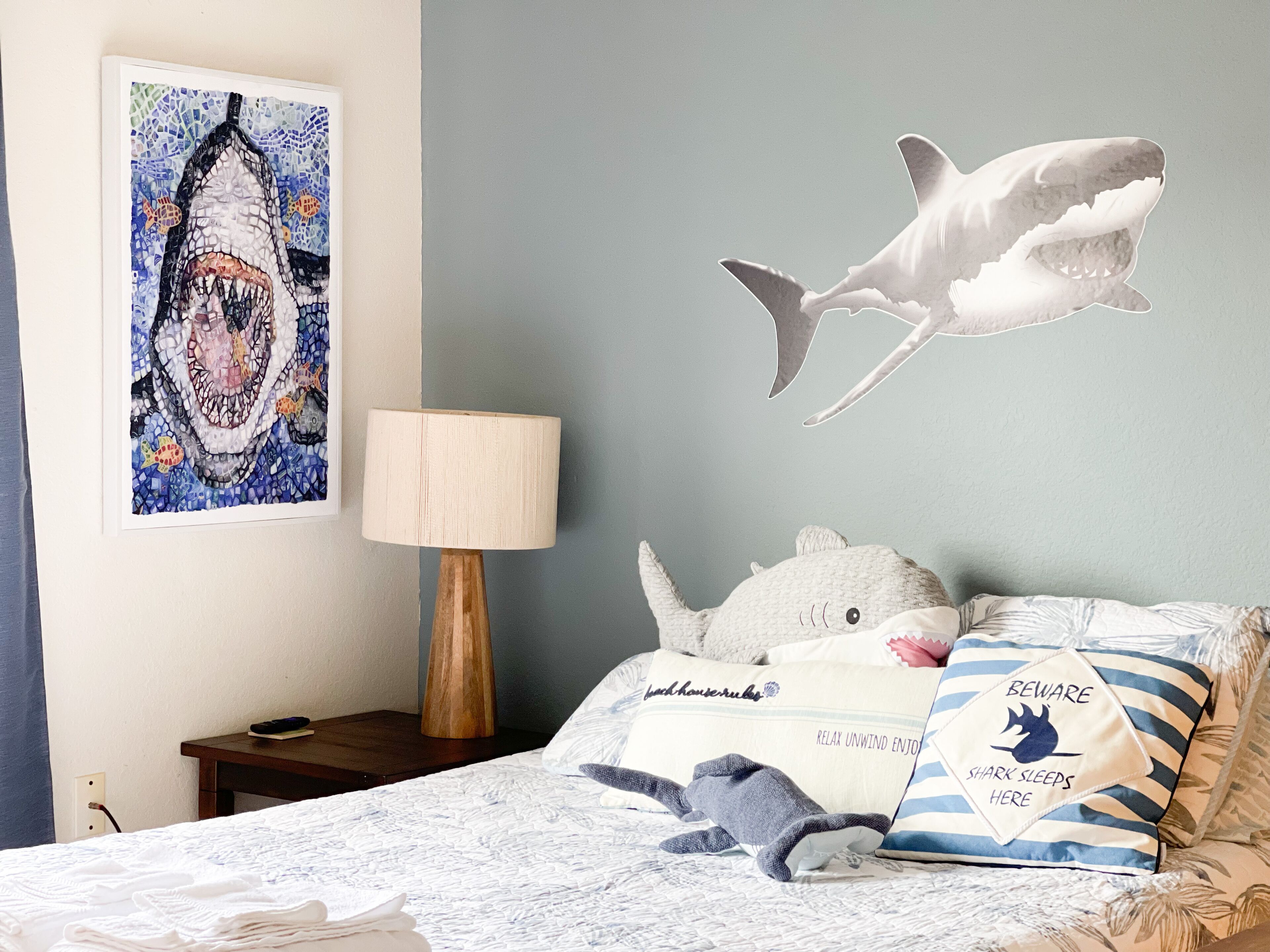 Un dormitorio con cama, mesita de noche, lámpara y un mural de un tiburón.