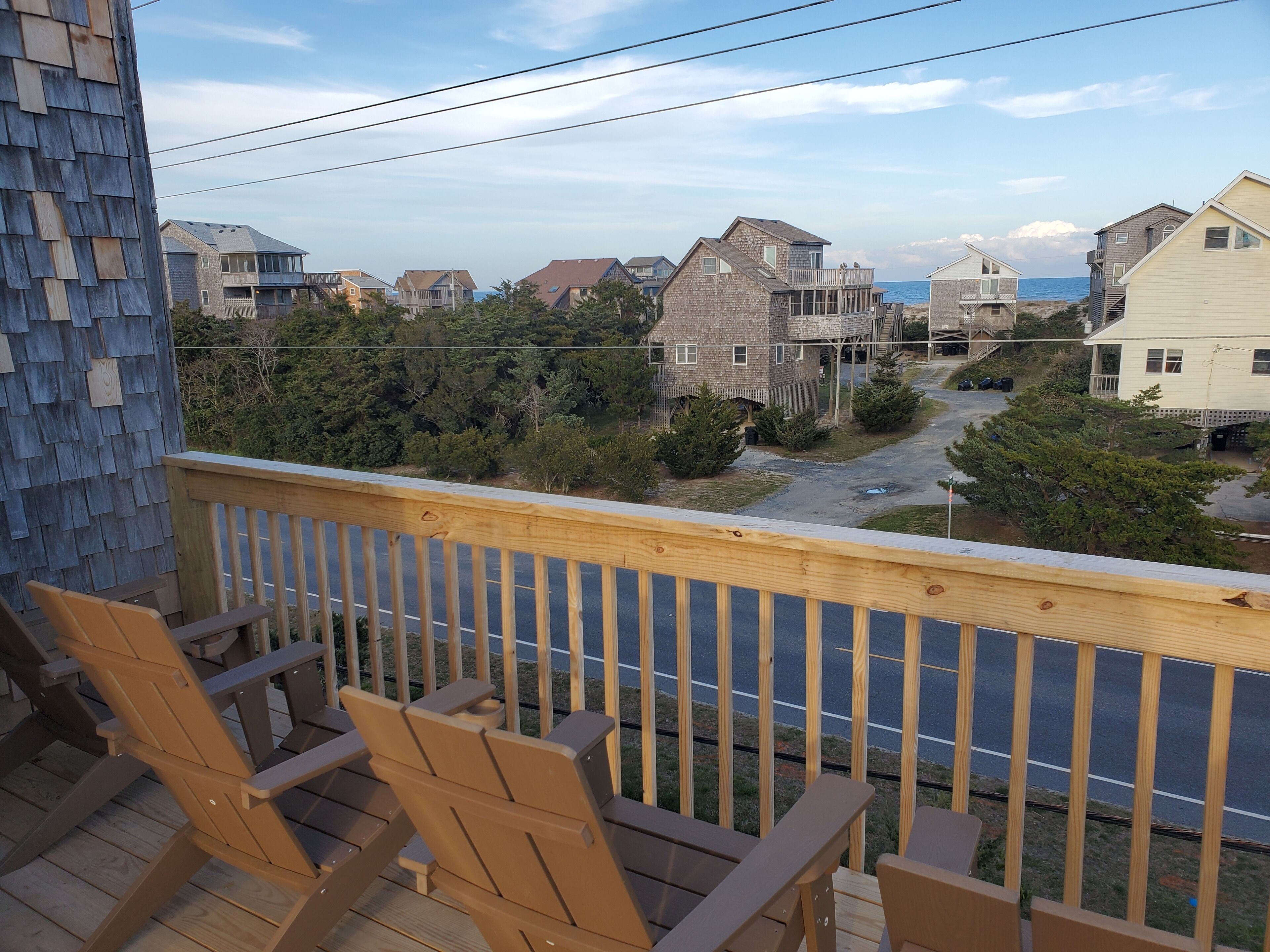 A wooden deck with chairs overlooking a residential area with houses and a road.