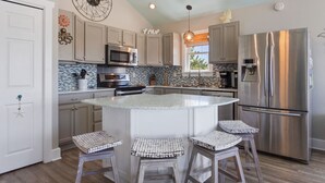 A modern kitchen with a central island, stainless steel appliances, and a decorative sun wall. - 6138 Island Life Cottage * 1 Mile to Beach (Nags Head)