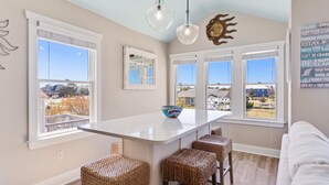 A kitchen with a large island, wicker bar stools, and a view of the neighborhood. - 6138 Island Life Cottage * 1 Mile to Beach (Nags Head)