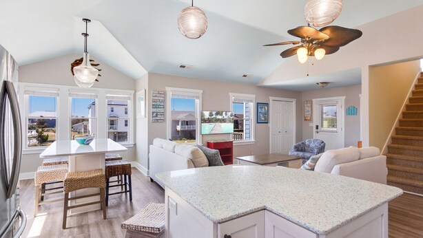 A spacious kitchen with a large island, white cabinetry, and a view of the outdoors through large windows. - 6138 Island Life Cottage * 1 Mile to Beach (Nags Head)