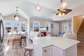 A spacious kitchen with a large island, white cabinetry, and a view of the outdoors through large windows.