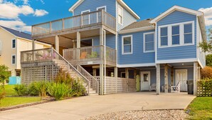 A two-story residential building with a balcony on the upper floor, a covered porch on the ground floor, and a driveway leading to the entrance. - 6138 Island Life Cottage * 1 Mile to Beach (Nags Head)