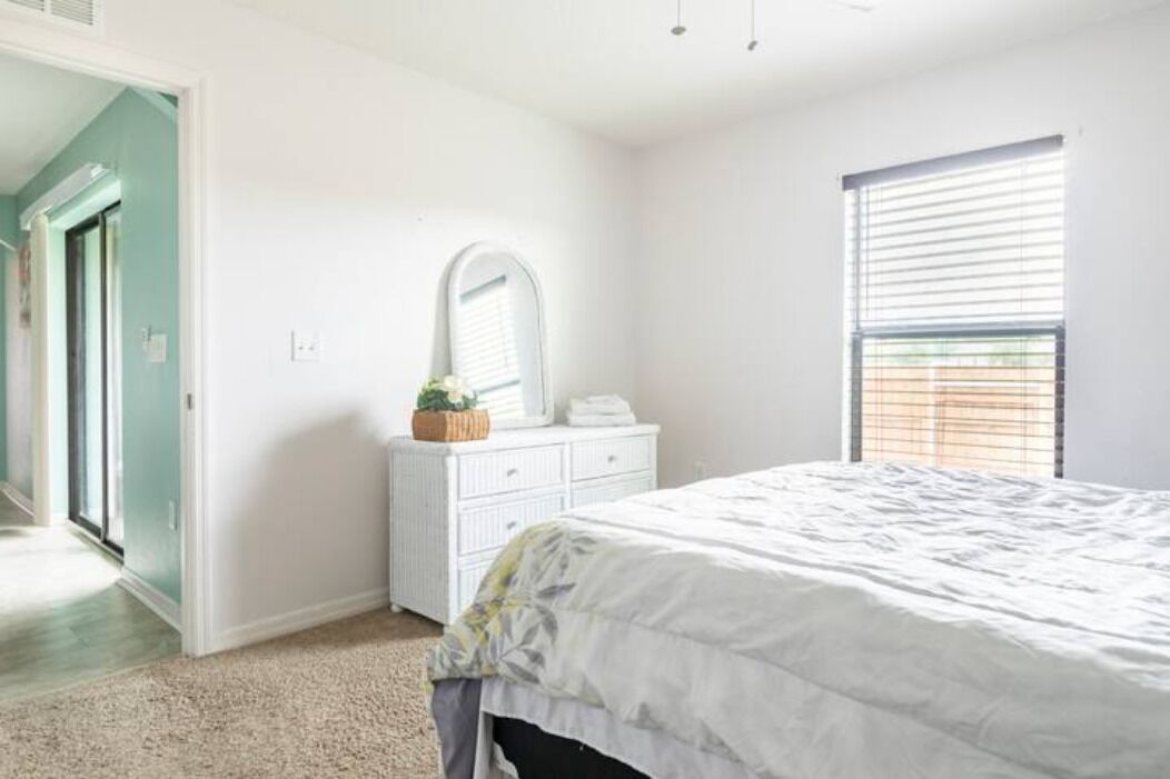 A bedroom with a bed, a dresser, a mirror, and a window with blinds.