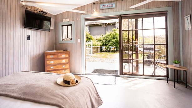 A bedroom with a bed, a dresser, a television, and a sliding glass door leading to an outdoor patio. - A Fantastic Location
"Just a short walk down the footpath opposite to the Beach" (Snells Beach)