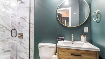 Un baño con ducha de mármol, inodoro, lavabo con espejo y tocador.