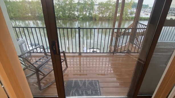 Une terrasse en bois avec une rambarde en métal donnant sur un lac. Un tapis sur le plancher porte l’inscription : « Détendez-vous, vous êtes au bord du lac. »