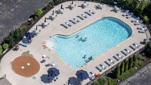 Vue aérienne d’un espace piscine avec des chaises longues, des parasols et un jacuzzi circulaire.