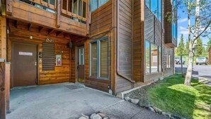 Un edificio de madera de dos pisos con base de piedra, una puerta metálica y un pequeño muro de piedra al frente.