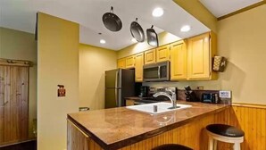 Una cocina con armarios de madera, encimera de granito, lavabo, microondas y refrigerador.
