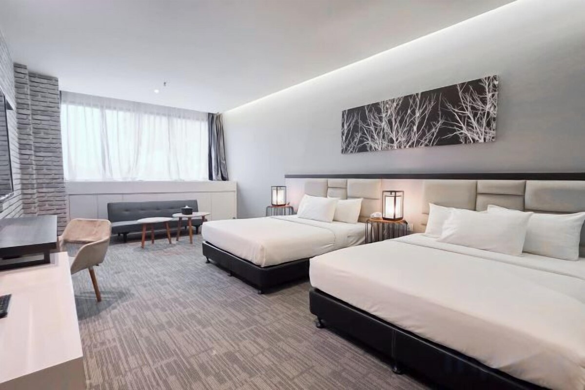 A hotel room with two beds, a desk, a chair, and a large window.