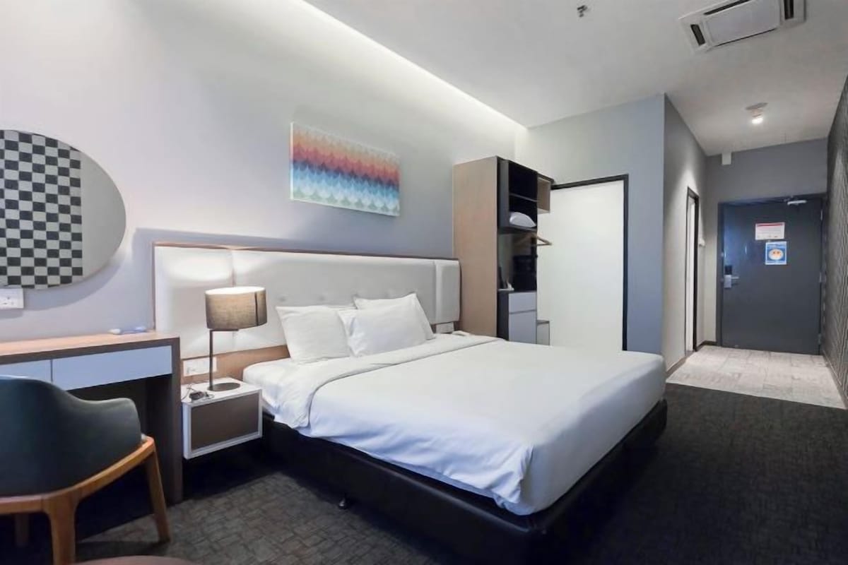 A modern hotel room with a large bed, a desk, a chair, and a wardrobe.