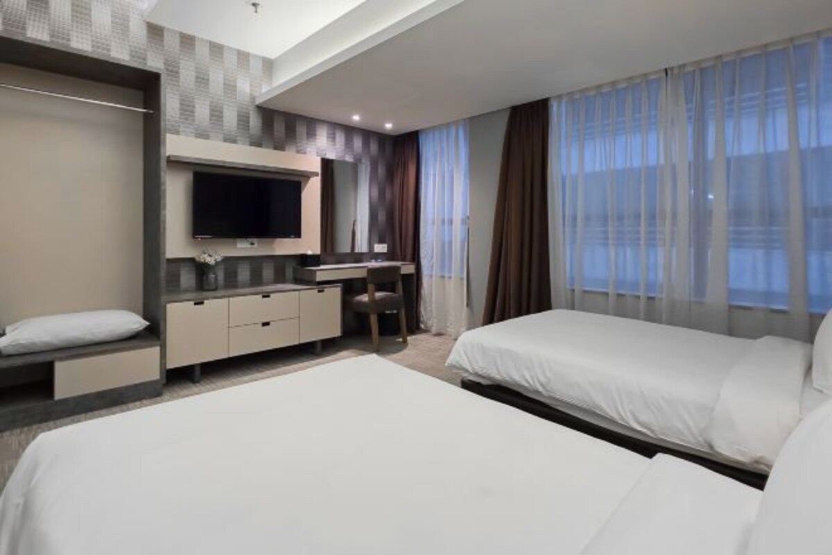 A hotel room with a bed, a desk, a TV, and a window with curtains.