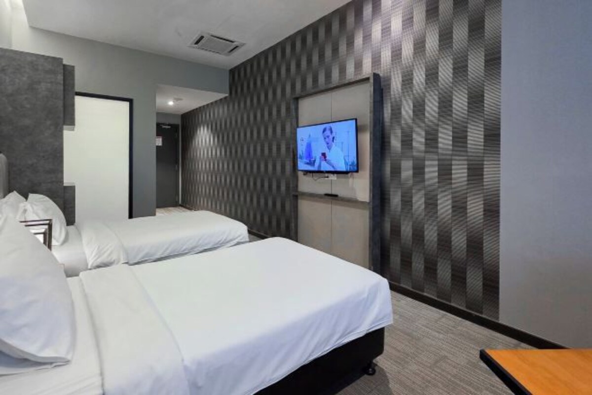 A hotel room with two beds, a TV mounted on the wall, and a wooden side table.