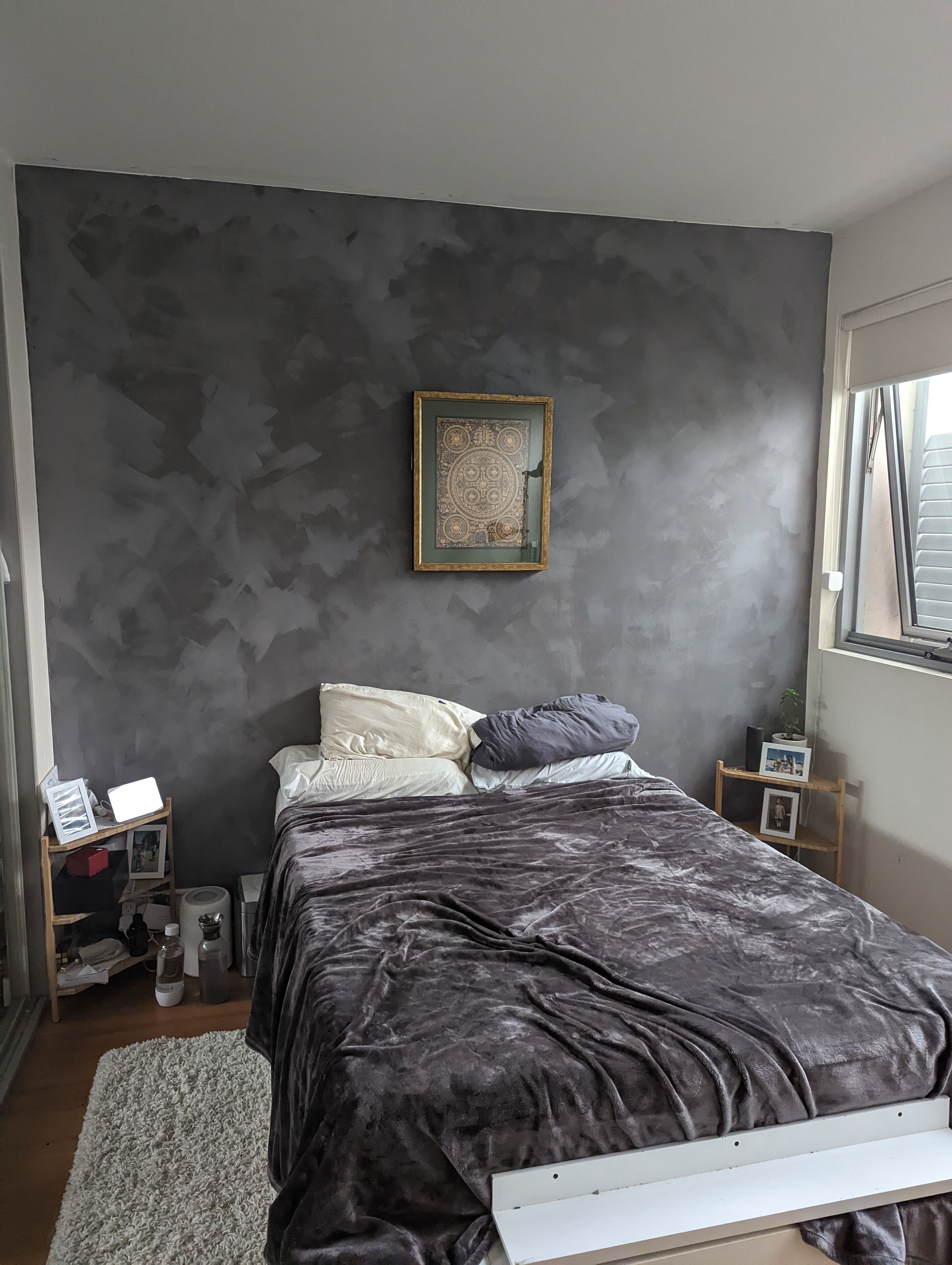 Une chambre à coucher avec un lit, une table de chevet, un cadre photo fixé au mur et une fenêtre.