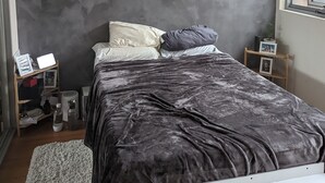 Un dormitorio con cama, mesita de noche, un cuadro en la pared y una ventana.