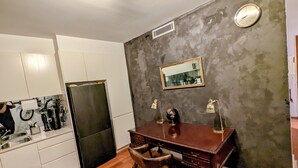 Una cocina compacta con armarios blancos, un refrigerador negro, un escritorio de madera con dos lámparas y un espejo en la pared.