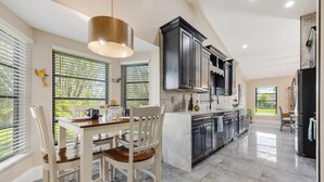 Una cocina moderna con una isla central, armarios oscuros y ventanas amplias.