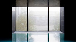Ein modernes Interieur mit spiegelndem Boden, einem großen Fenster mit vertikalen Jalousien und einer Betonwand.
