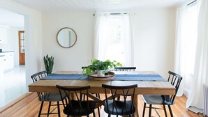 Uma sala de jantar com mesa de madeira, cadeiras pretas, um vaso com planta e um espelho na parede.