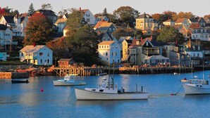 Um porto com várias embarcações atracadas, rodeado por casas com varandas e um cais que se estende sobre a água.