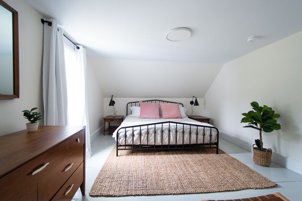 A bedroom with a bed, bedside tables, a dresser, and a large woven rug.
