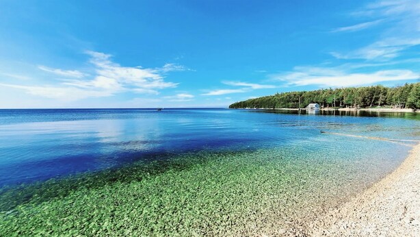 A clear lake with a sandy beach and a forested island. - Perfect Retreat for 2 | Studio Above Bakery, Dogs! (Sister Bay)