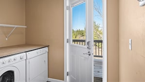 A laundry room with a washer and dryer, a wooden shelf, and a door leading to an outdoor deck. - Perfect Retreat for 2 | Studio Above Bakery, Dogs! (Sister Bay)