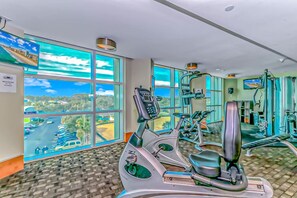 A gym with exercise equipment, large windows, and a view of a road and greenery.