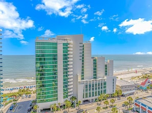 A modern hotel with a prominent glass facade, a beach view, and a parking area.
