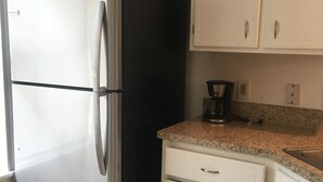 Una cocina con un refrigerador de acero inoxidable, un horno negro, armarios blancos, una encimera de granito y una cafetera.