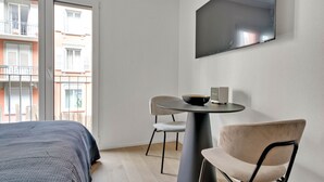 Moderni hotellihuone, jossa on sänky, pyöreä pöytä, jossa on kulho ja kaiutin, tuoli sekä seinälle asennettu televisio.