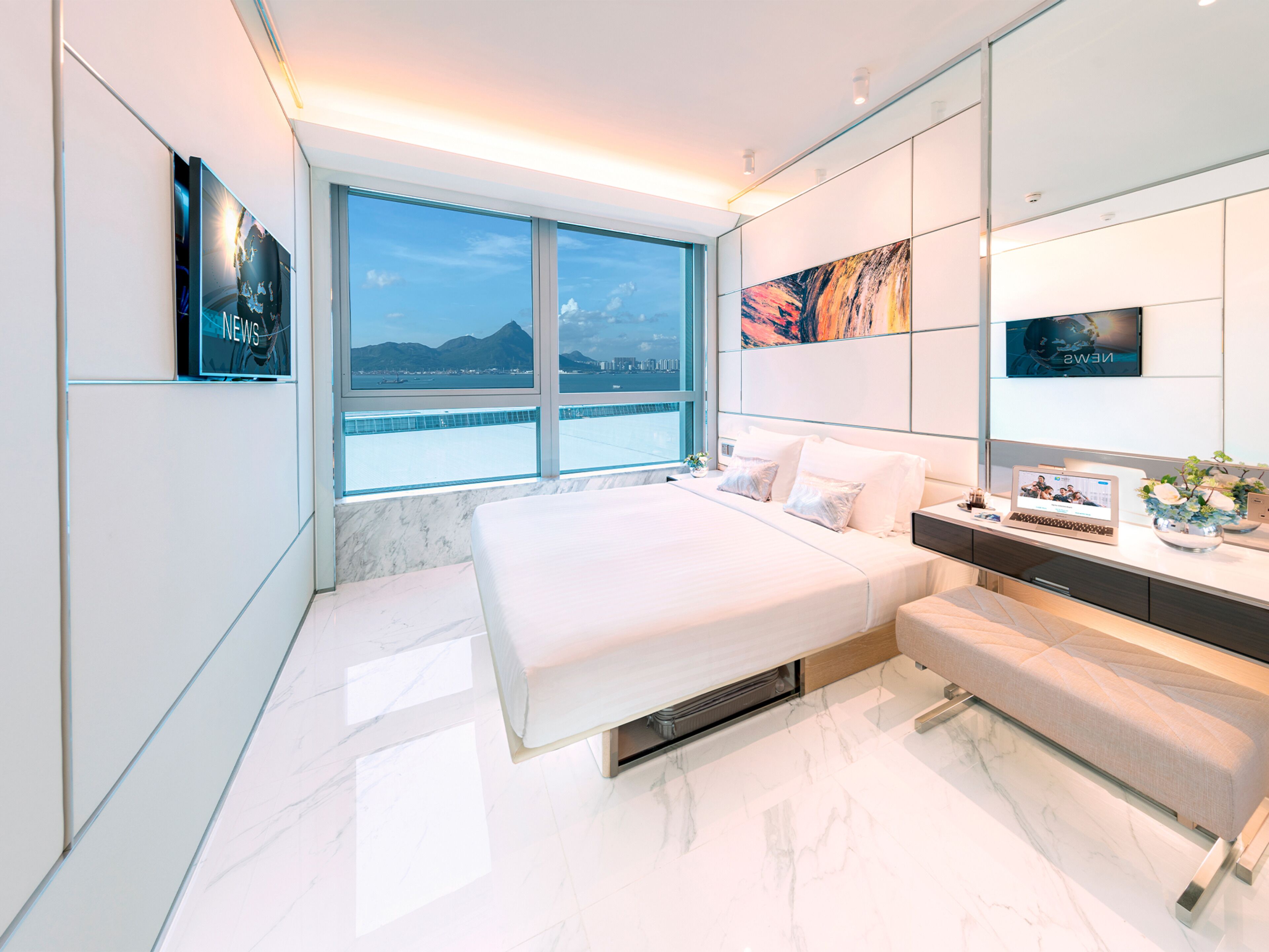 A modern bedroom with a large bed, a desk, and a view of the water.